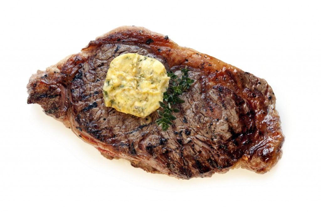 Steak topped with herb butter and thyme, isolated on white.