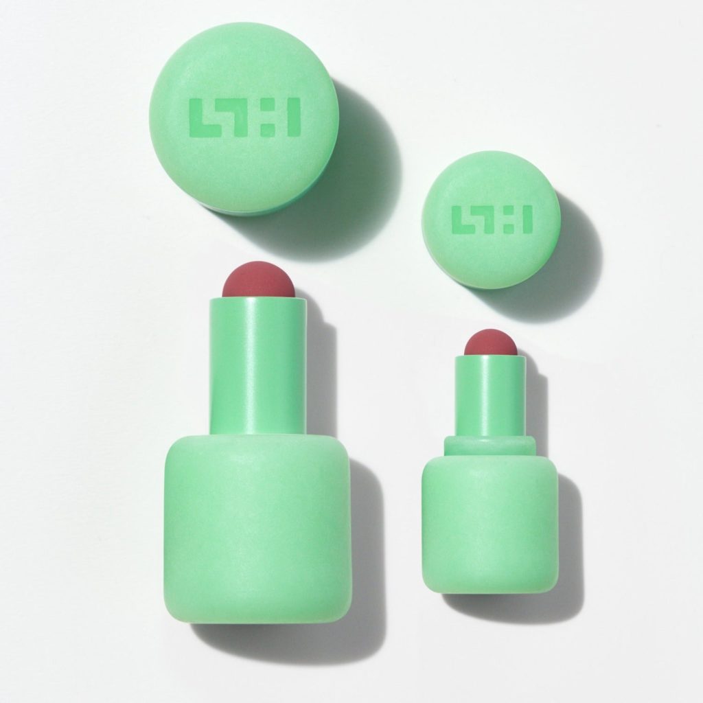 Lipsticks in rounded green packaging. The lipstick is a dark pink.